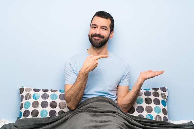 Homme au lit, tenant une surface imaginaire sur la paume pour insérer une annonce
