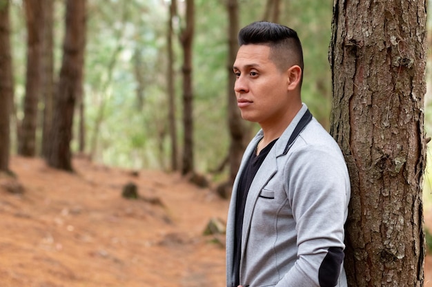 Homme au look sexy vêtu d'un blazer gris, dans une forêt de tons orangés