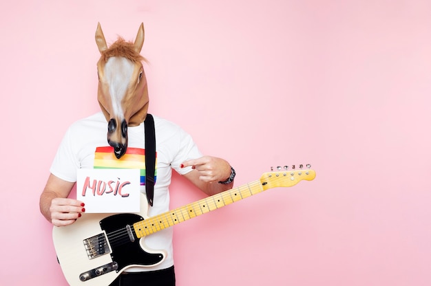 L'homme au masque de cheval et à la guitare électrique pointe vers un panneau qui dit musique