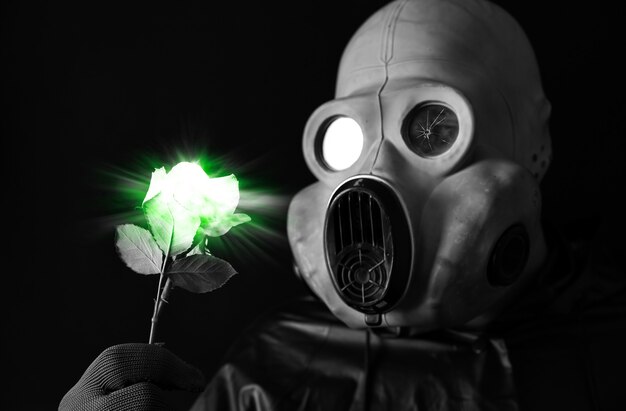 Homme au masque à gaz tenant une fleur lumineuse verte. Influence du rayonnement. Pollution environnementale. Notion de Tchernobyl. Une énergie nucléaire dangereuse. Désastre écologique.