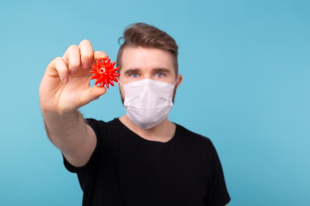 Homme au masque médical tenant une boule de Covid rouge