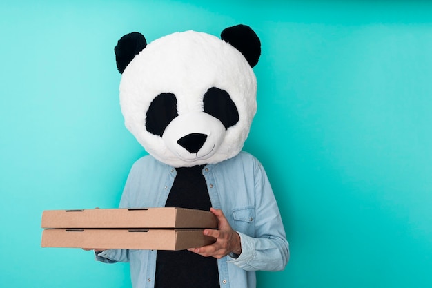 Homme au masque de panda tenant deux boîtes à pizza isolées sur un mur bleu