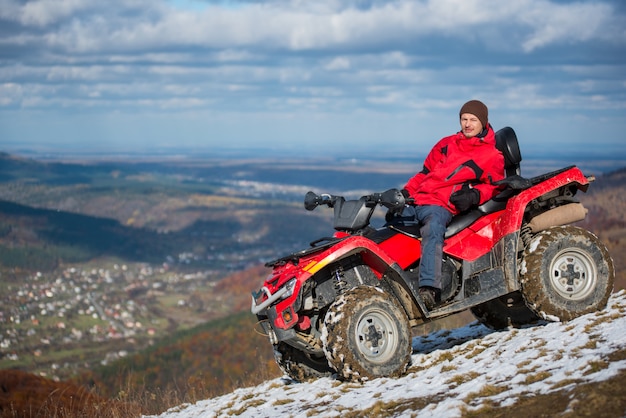 Homme au repos sur un vélo de VTT rouge au sommet d'une montagne enneigée