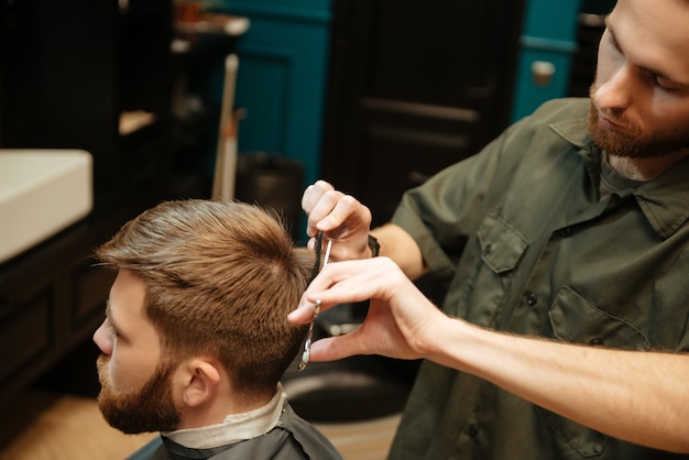 L'homme au salon de coiffure se coupe les cheveux par le coiffeur avec des ciseaux alors qu'il était assis sur une chaise.