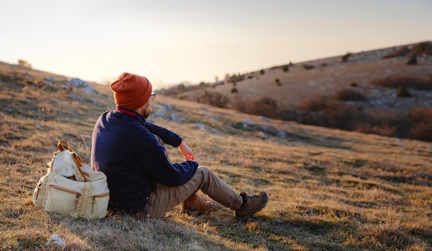 Un homme au sommet d'une falaise dans les montagnes printanières au coucher du soleil et profitant de la vue sur la nature