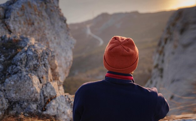 Un homme au sommet d'une falaise dans les montagnes printanières au coucher du soleil et profitant de la vue sur la nature