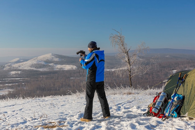 Un homme au sommet de la montagne regarde à travers des jumelles. Il se tient près de la tente le matin sur