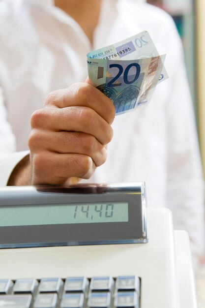 un homme au supermarché debout près de la caisse en espèces et tenant 20 euros