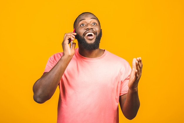 Homme au téléphone. Gai homme noir parlant au téléphone mobile et souriant en se tenant isolé sur fond jaune.