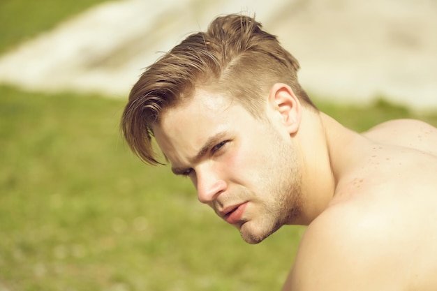 L'homme au visage sérieux et à la coiffure élégante regarde de côté sur fond d'herbe verte