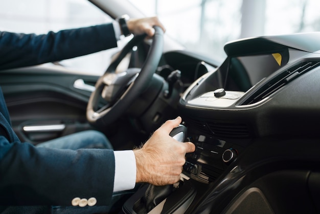 Homme au volant d'une nouvelle automobile chez un concessionnaire automobile. Client dans la salle d'exposition de véhicules, homme achetant des transports, entreprise de concessionnaire automobile