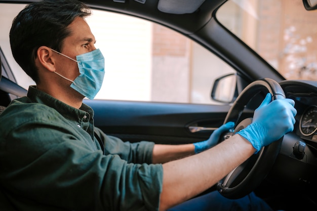 Un homme au volant d'une voiture met un masque médical lors d'une épidémie, protection contre le virus