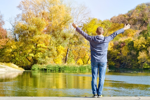 Homme aux bras levés debout sur le quai Automne ensoleillé Vue arrière