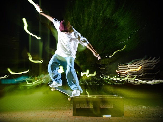 Photo homme aux bras tendus faisant du skateboard contre des peintures légères dans le parc la nuit