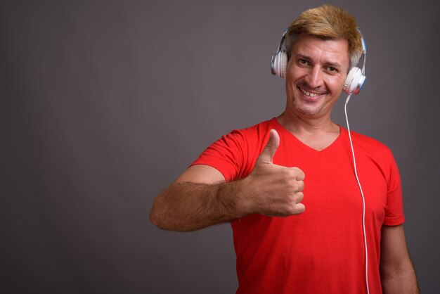 Homme aux cheveux blonds, écouter de la musique contre le mur gris