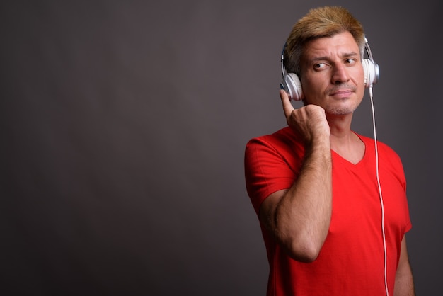 Homme aux cheveux blonds, écouter de la musique contre le mur gris