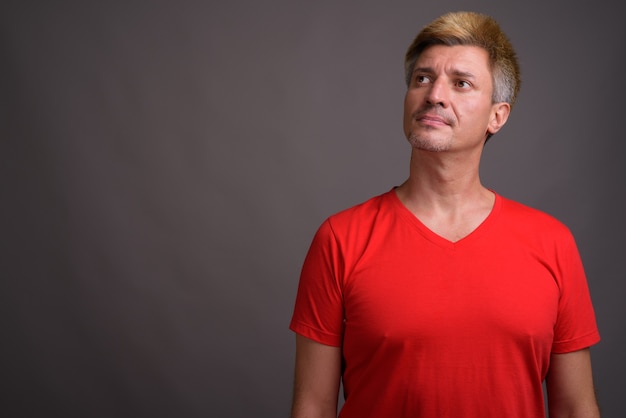 Homme aux cheveux blonds portant une chemise rouge contre le mur gris