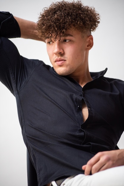 Un homme aux cheveux bouclés porte une chemise noire sur fond blanc.