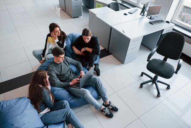 L'homme aux cheveux courts tape sur le clavier. Groupe de jeunes en vêtements décontractés travaillant dans le bureau moderne