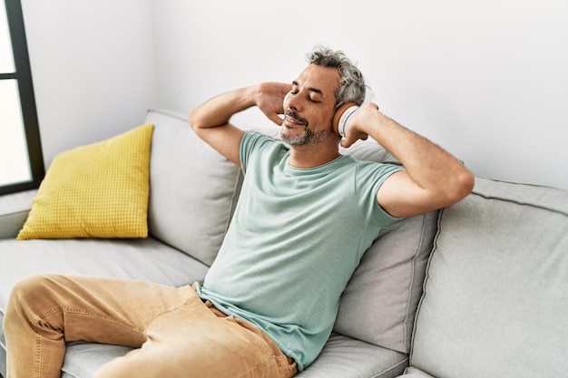 Homme aux cheveux gris d'âge moyen écoutant de la musique assis sur un canapé à la maison