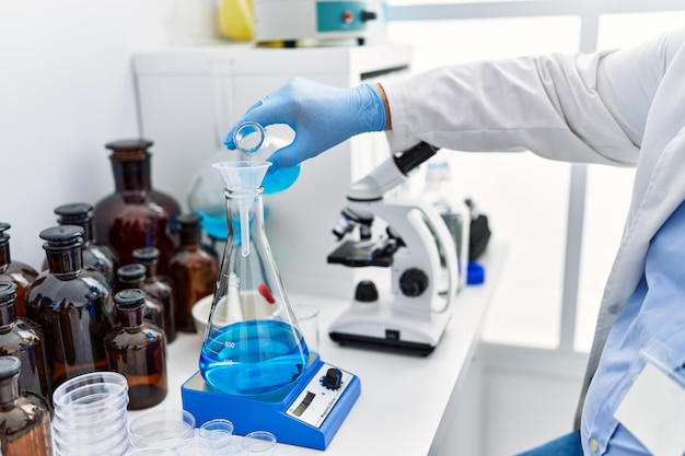 Homme aux cheveux gris d'âge moyen portant un uniforme de scientifique versant du liquide sur un tube à essai au laboratoire