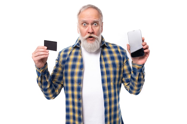 Homme aux cheveux gris mature intelligent avec une barbe dans une chemise avec une carte et une maquette de téléphone sur un blanc