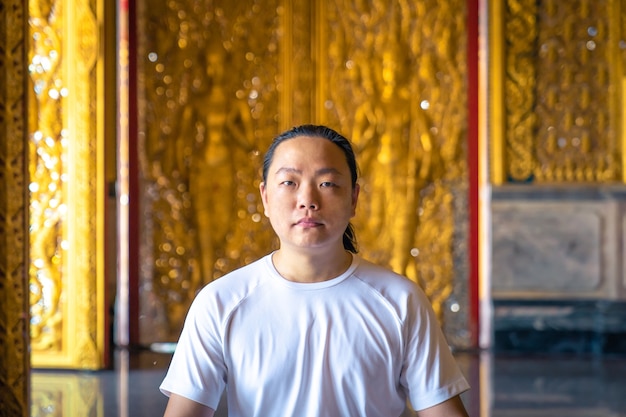 L'homme aux cheveux longs asiatique se détend de la méditation avec tout le costume blanc s'asseoir devant le papier peint d'or de Bouddha dans le Temple, en Thaïlande.