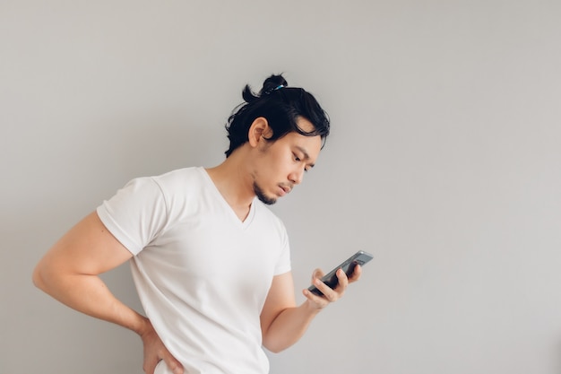 Homme aux cheveux longs en t-shirt décontracté blanc utilise un smartphone