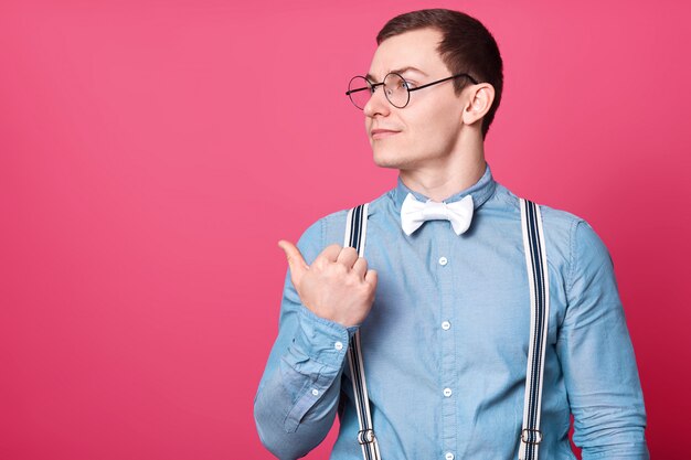 Homme aux cheveux noirs à la mode attentif regarde de côté, pointant avec son pouce, semble concentré