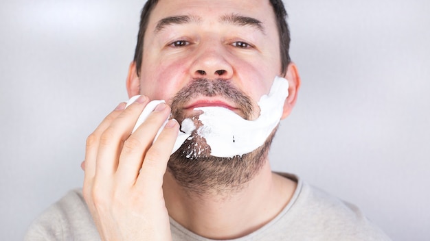 Homme aux cheveux noirs de race blanche appliquant de la mousse à raser pour sa barbe en regardant la caméra en souriant