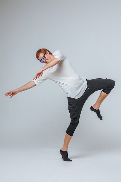 Homme aux cheveux rouges dans des lunettes de soleil et un t-shirt blanc dansant sur un fond clair