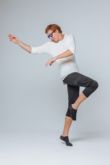 Homme aux cheveux rouges dans des lunettes de soleil et un t-shirt blanc posant sur un fond clair