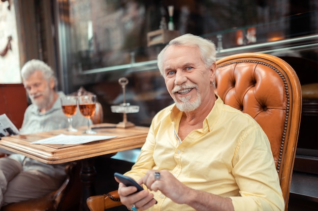 Homme aux yeux bleus. Homme retraité aux yeux bleus tenant un smartphone tout en passant du temps avec un ami