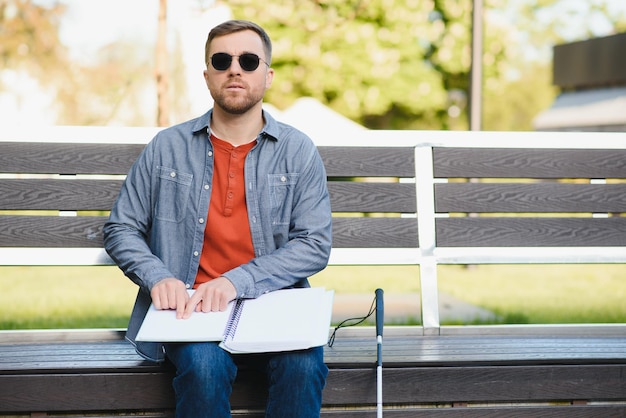 Homme aveugle lisant un livre en braille assis sur un banc dans un parc d'été au repos