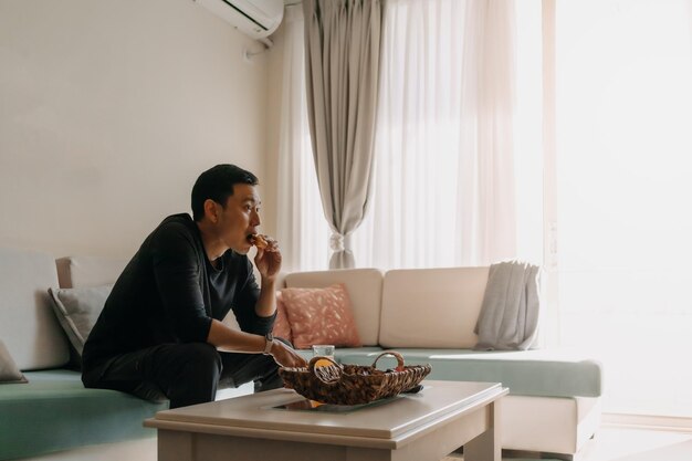 Homme ayant du pain et du jus comme petit-déjeuner sur le canapé du salon