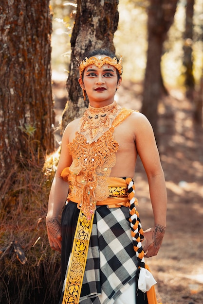 Homme balinais debout dans la forêt tout en portant une couronne en or et un collier en or