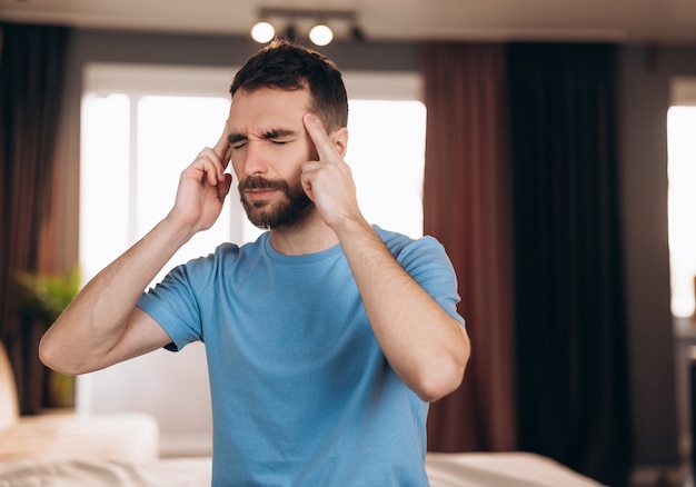 Homme avec barbe assis dans son lit à la maison souffrant de maux de tête ou de gueule de bois