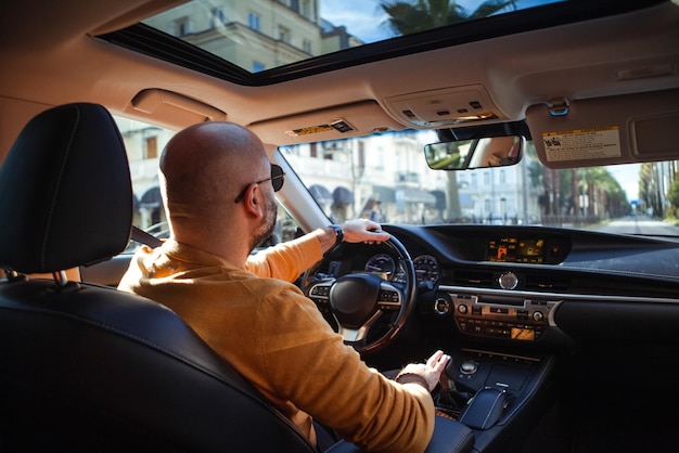 Un homme à la barbe chauve d'âge moyen conduit une voiture.