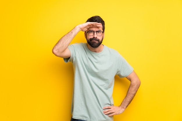 Homme à la barbe et à la chemise verte, regardant au loin avec la main pour regarder quelque chose