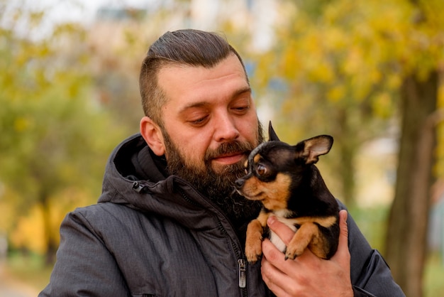 Photo homme avec barbe et chihuahua. un homme dans le parc avec son animal de compagnie bien-aimé dans ses bras. guy avec chien