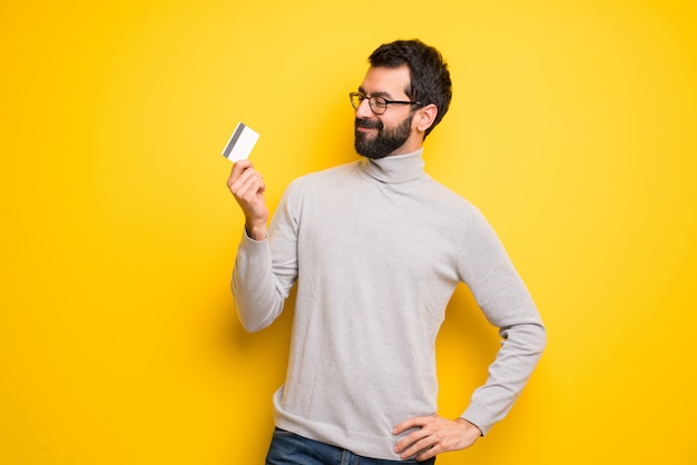 Homme avec barbe et col roulé tenant une carte de crédit et de penser