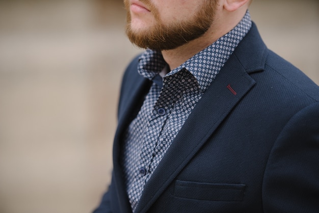 Un homme avec une barbe en costume bleu pose dans la rue pour faire de la publicité pour les vêtements pour hommes.