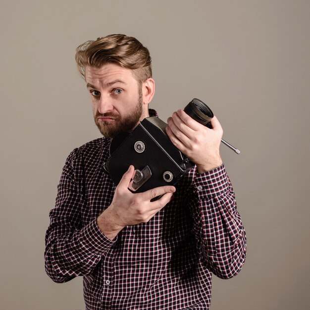 Homme barbe dans une chemise à carreaux tient dans les mains d'une vieille caméra