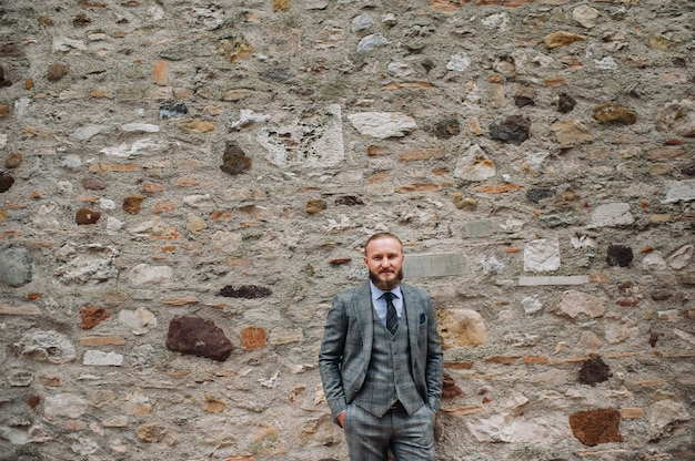 Un homme avec une barbe dans un costume trois pièces gris strict avec une cravate dans la vieille ville de Sirmione, un homme élégant dans un costume gris en Italie.