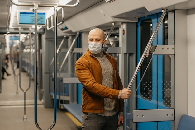 Un homme avec une barbe dans un masque médical pour éviter la propagation du coronavirus tient la main courante dans une voiture de métro. Un homme chauve portant un masque chirurgical garde une distance sociale dans un train.