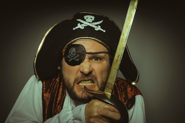 Photo homme à barbe habillé comme un pirate, avec cache-oeil et épée en acier