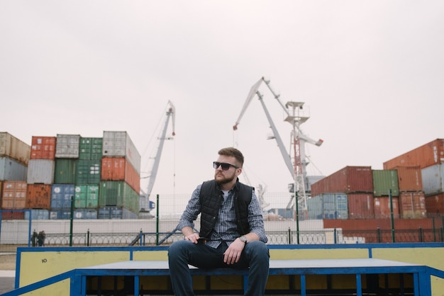 Un homme avec une barbe et des lunettes de soleil dans une chemise à carreaux et un gilet posant dans la rue