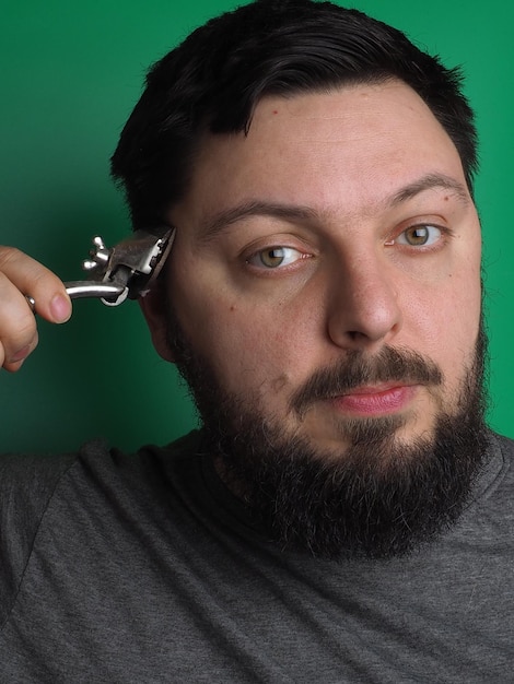 Un homme avec une barbe et une moustache tient une clé à son oreille.