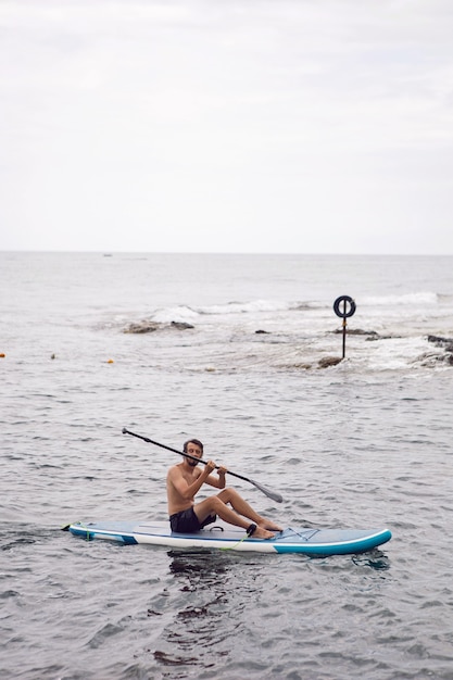 Un homme avec une barbe nage sur un stand up paddle sur un océan bleu calme. Sup surf dans l'eau