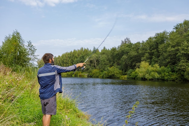 Un homme avec une barbe pêche sur la rivière en jetant une ligne